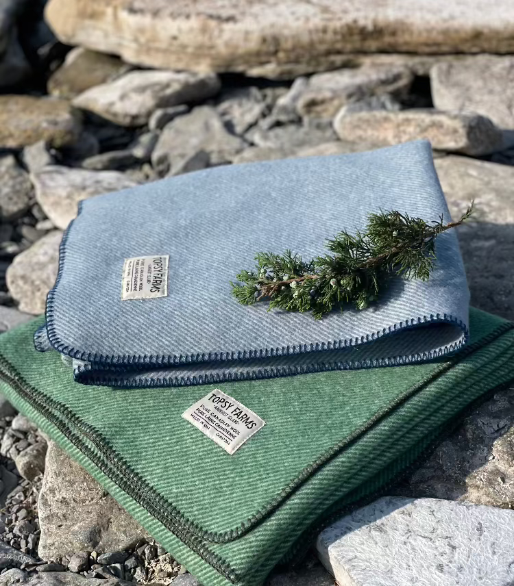 Topsy Farms' Canadian wool throws in blue and green on a rocky beach